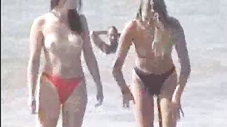 Due teen bionde camminano sulla sabbia in topless